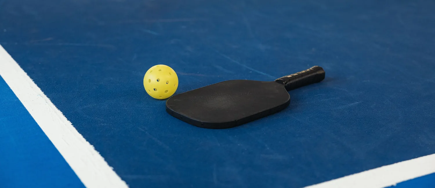 Yellow pickleball and paddle resting on a blue court